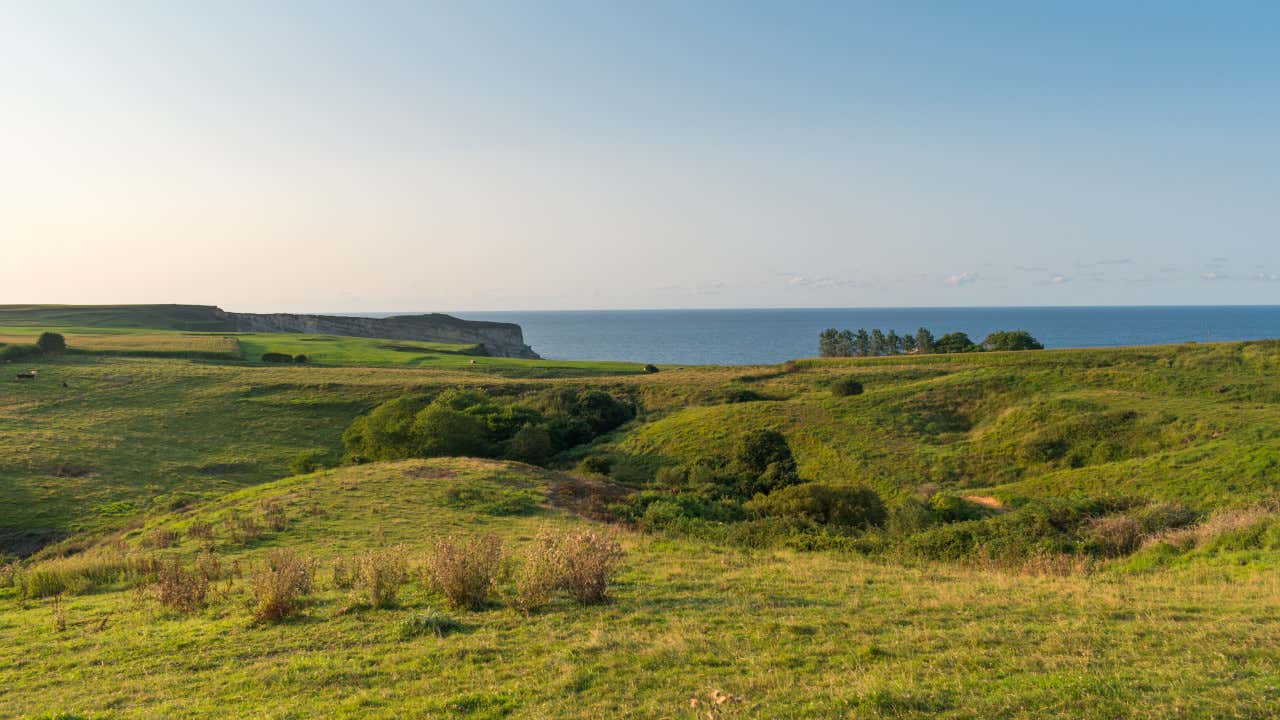 Paisagem da cornija cantábrica, com campos de distintos tons de verde e o mar ao fundo