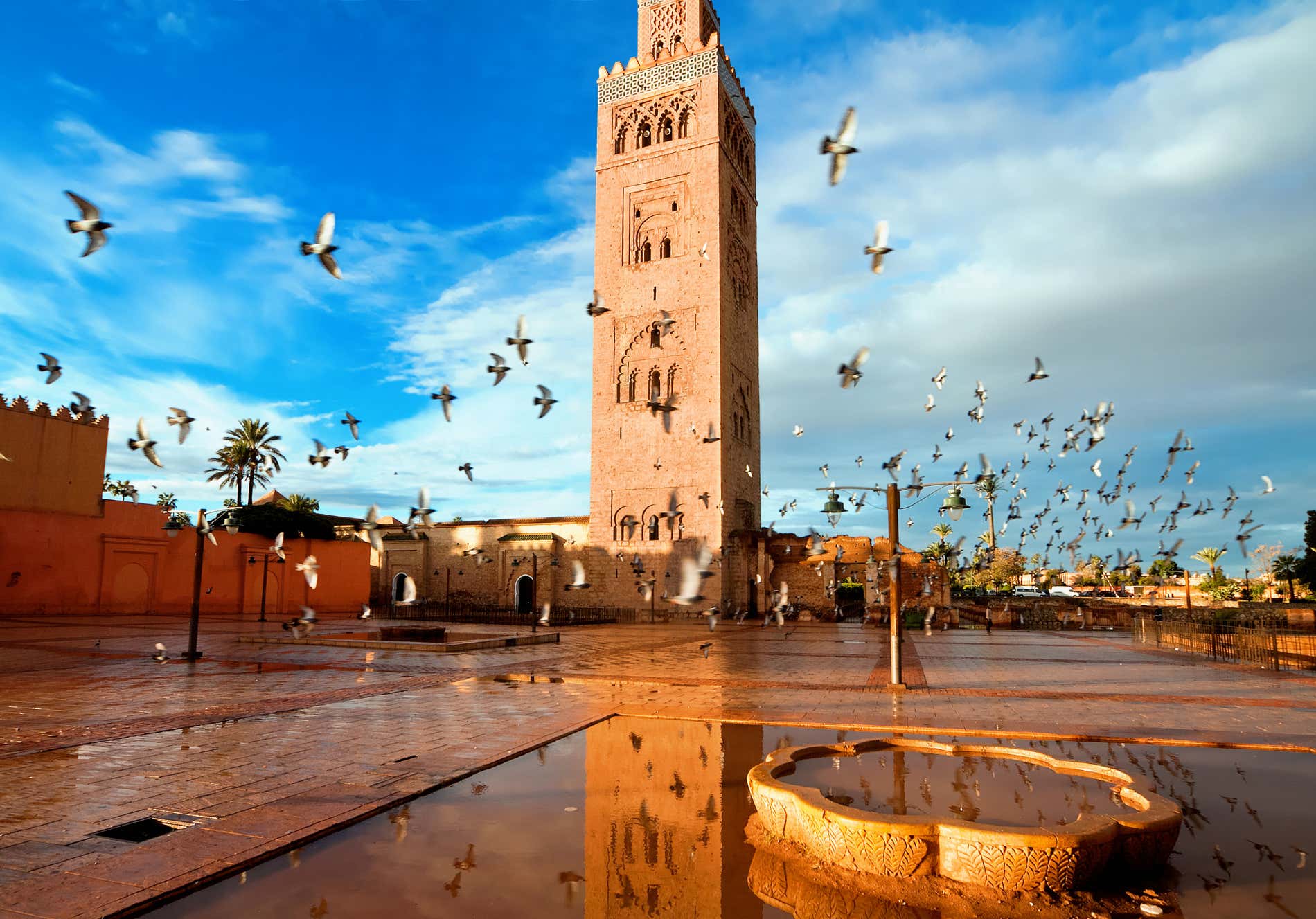 Piazza di Marrakech con un minareto e uno stormo di uccelli sotto un cielo poco nuvoloso