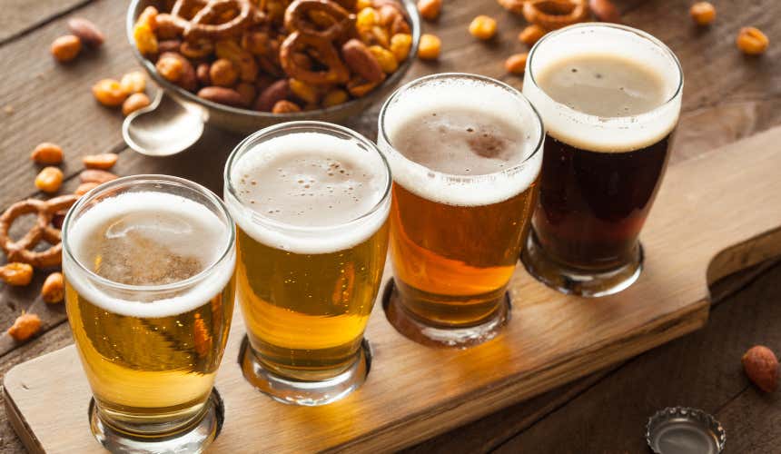 Varietà di birre in primo piano, su un vassoio di legno con salatini sullo sfondo