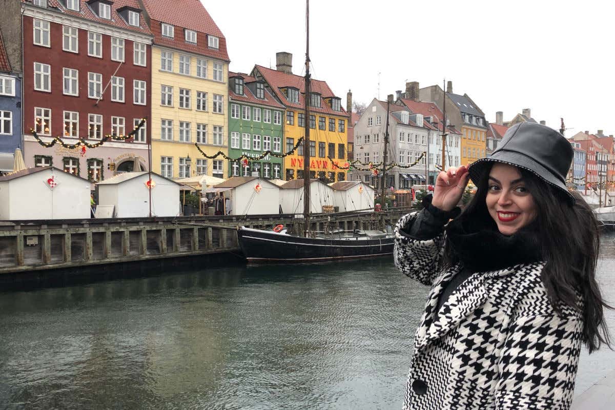 Karima El-Berjiji con un gorro y abrigo blanco y negro frente a las coloridas casas del canal de Nyhavn, en Copenhague