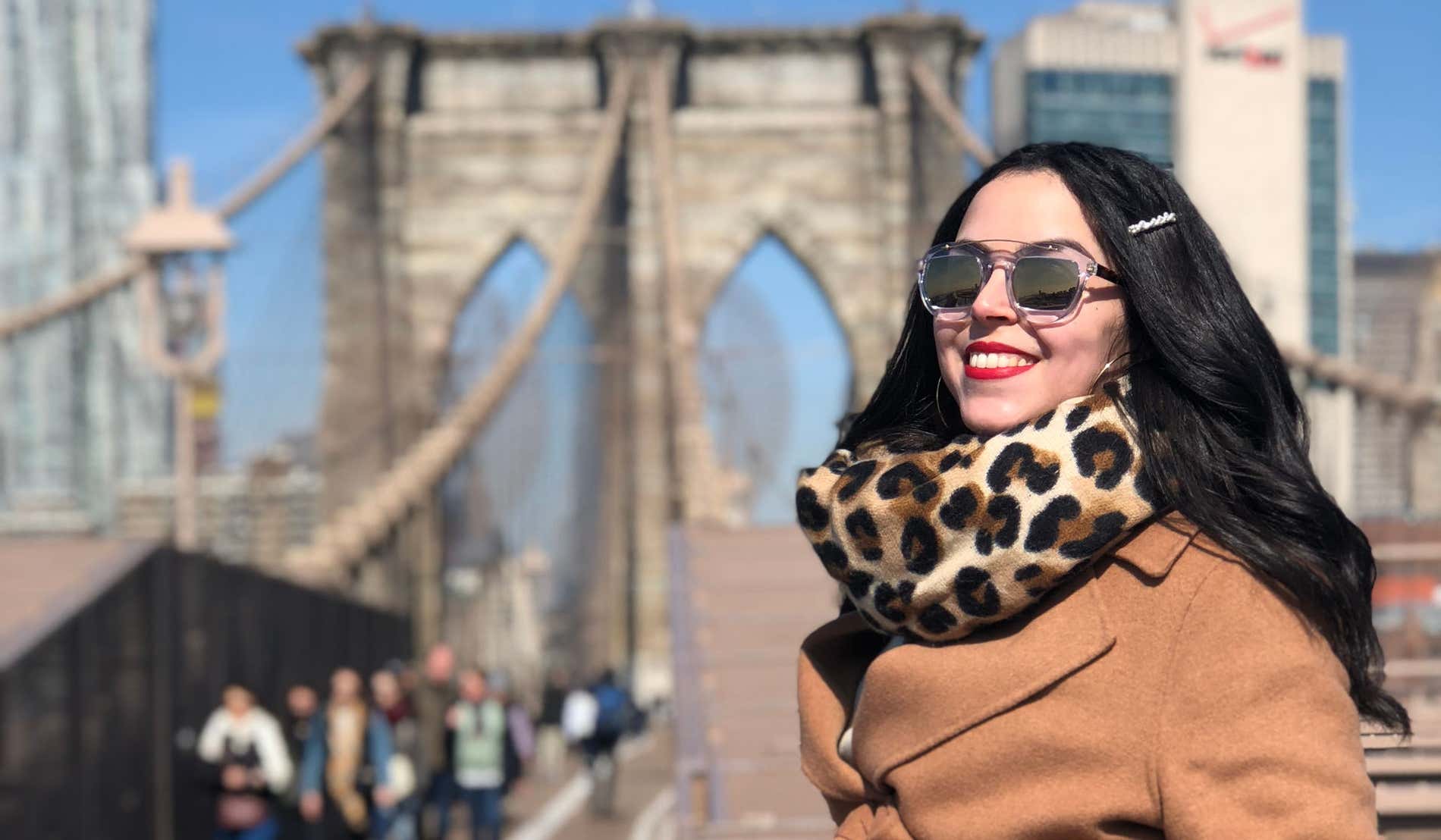Karima El-Berjiji posando con abrigo y gafas de sol en un día soleado junto al puente de Brooklyn, en Nueva York