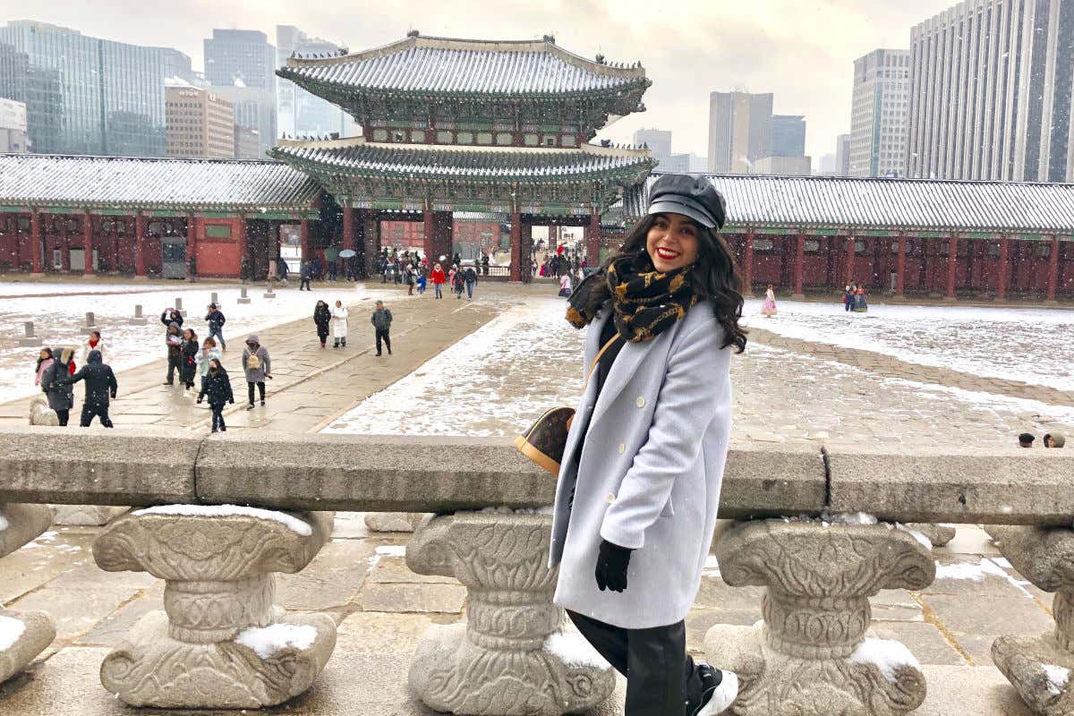 Karima El-Berjiji posando frente a un palacio de color rojo en Corea del Sur en un día nublado y con nieve