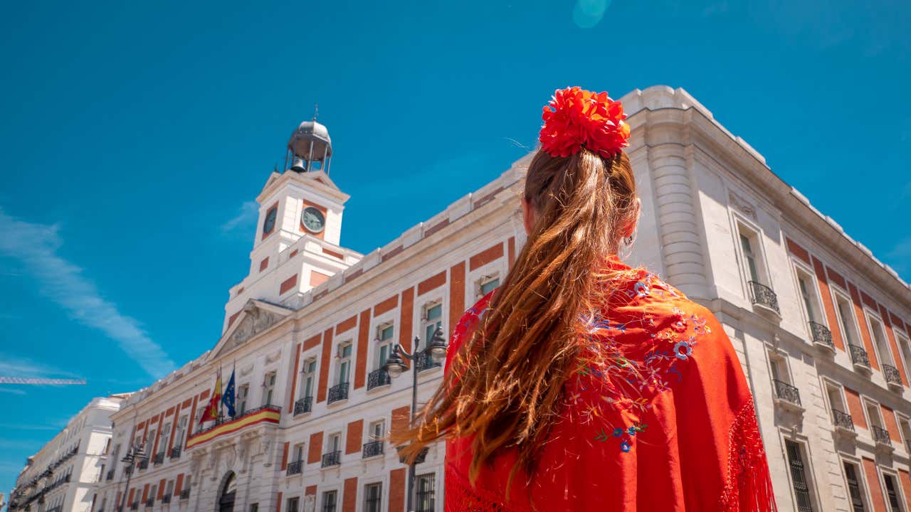 Una giovane donna vestita con gli abiti tradizionali per la festa di San Isidro a Madrid. Ripresa di spalle, indossa uno scialle rosso e porta un grosso fiore rosso sulla testa
