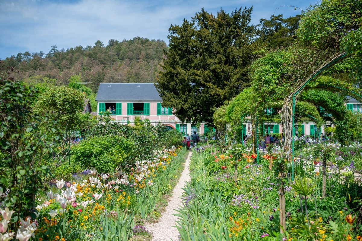 Maisons roses aux volets verts au milieu d'un jardin foisonnant plein de fleurs