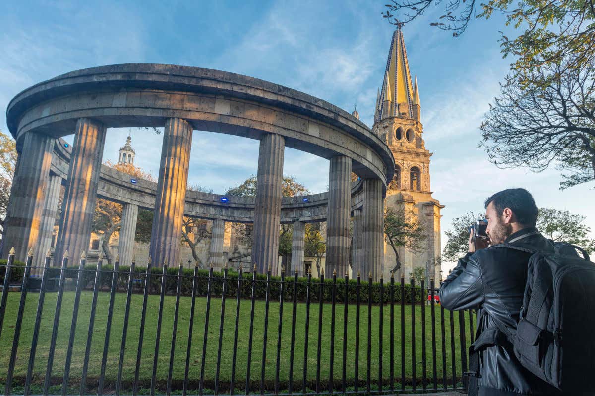 Un fotógrafo de espaldas inmortalizando la Rotonda de los Jaliscienses Ilustres y la catedral de Guadalajara al fondo