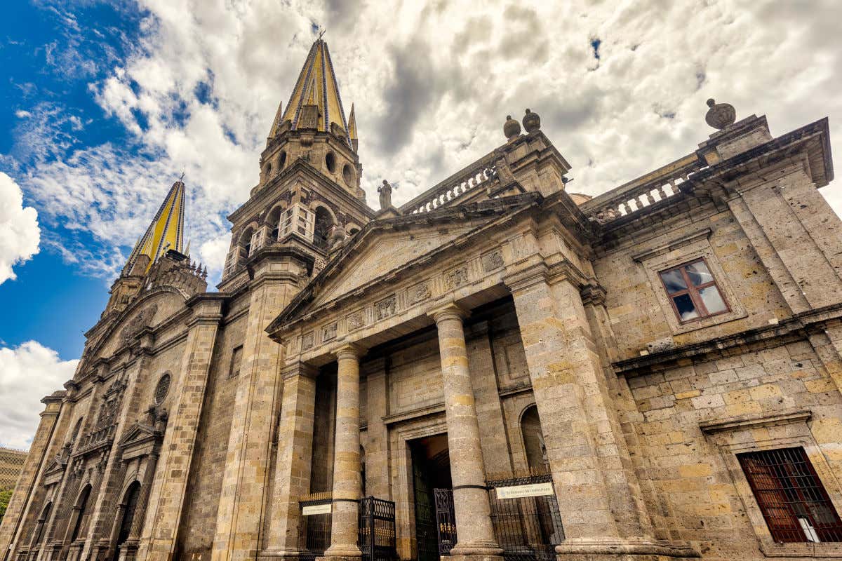 Panorámica de la fachada rupestre de la catedral de Guadalajara con sus dos torres triangulares en un día parcialmente nuboso