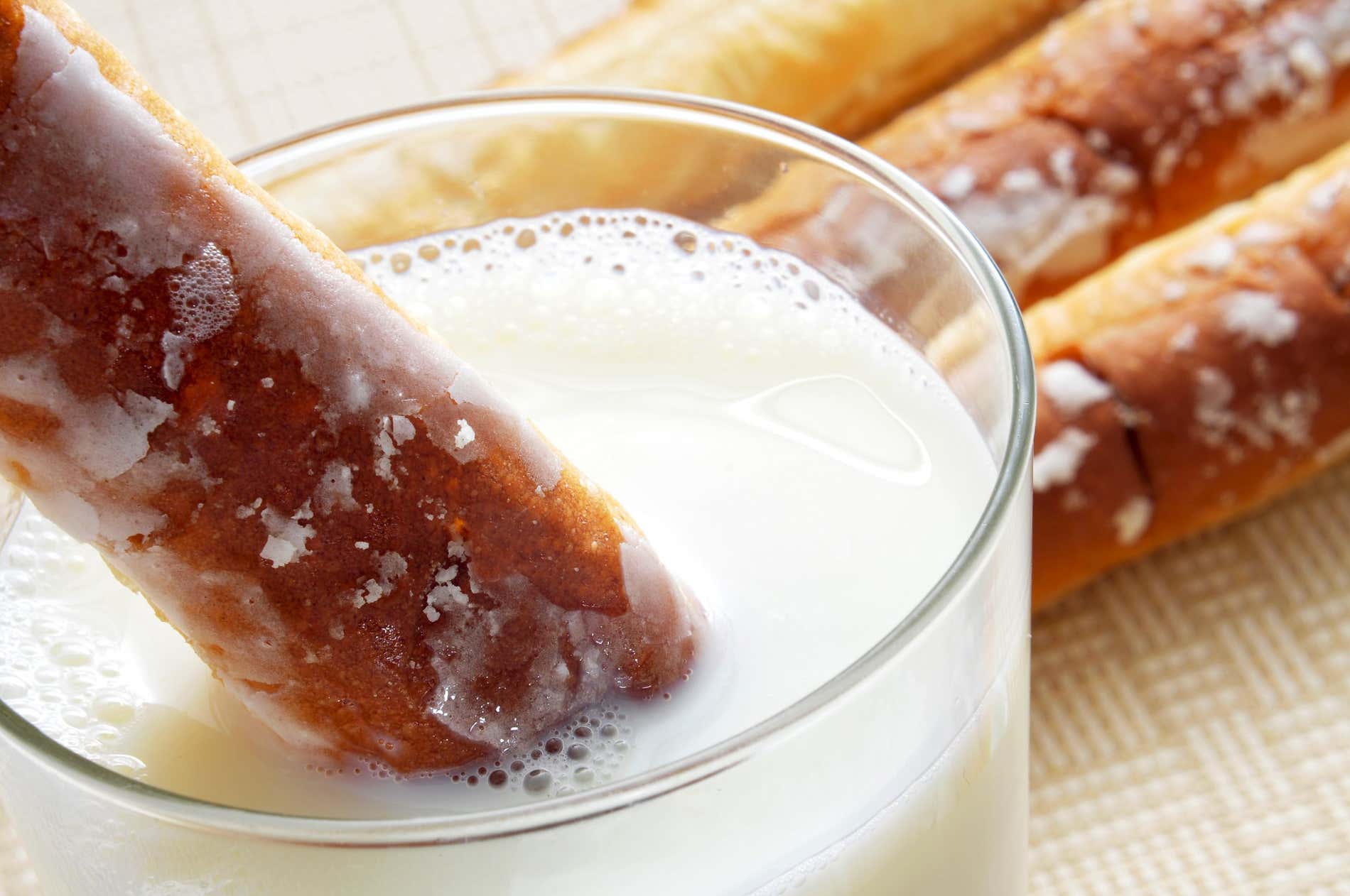 A close-up of a glass of white horchata with a farton dipped in, and other fartons behind