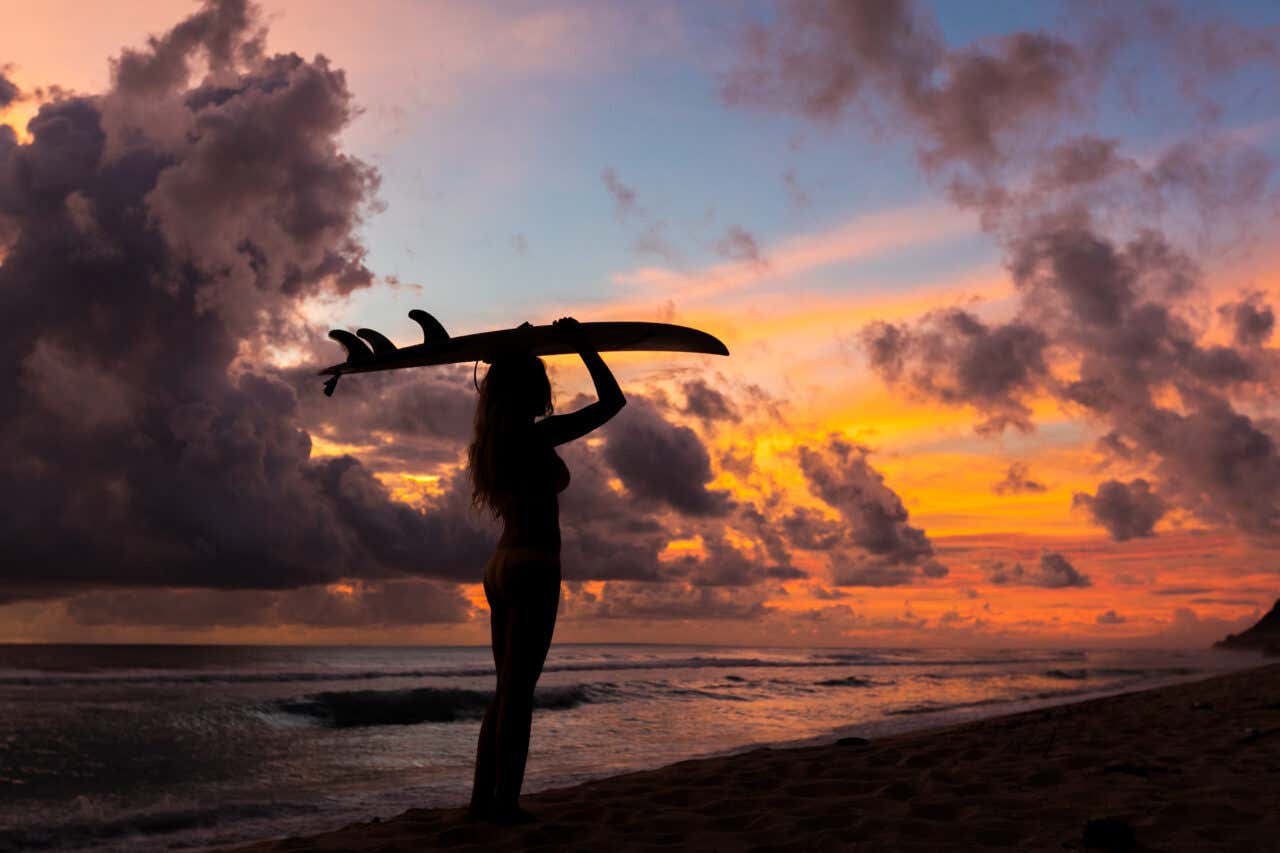 Surfeuse sur une plage avec sa planche de surf au coucher de soleil