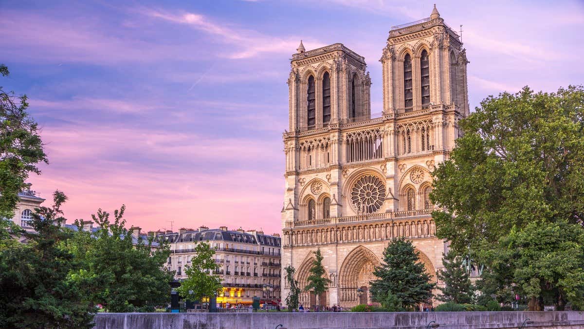 Cathédrale Notre-Dame de Paris au coucher du soleil, ciel bleu et rose, arbres verdoyants sur le parvis