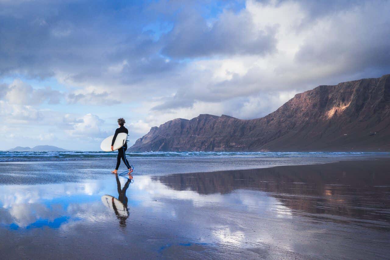 Surfeur avec sa planche de surf sous le bras sur une plage de sable noir à Lanzarote aux îles Canaries