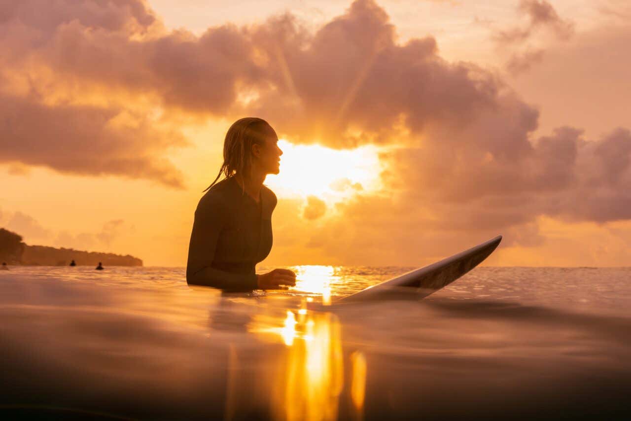 Surfeuse avec sa planche de surf dans la mer au coucher de soleil