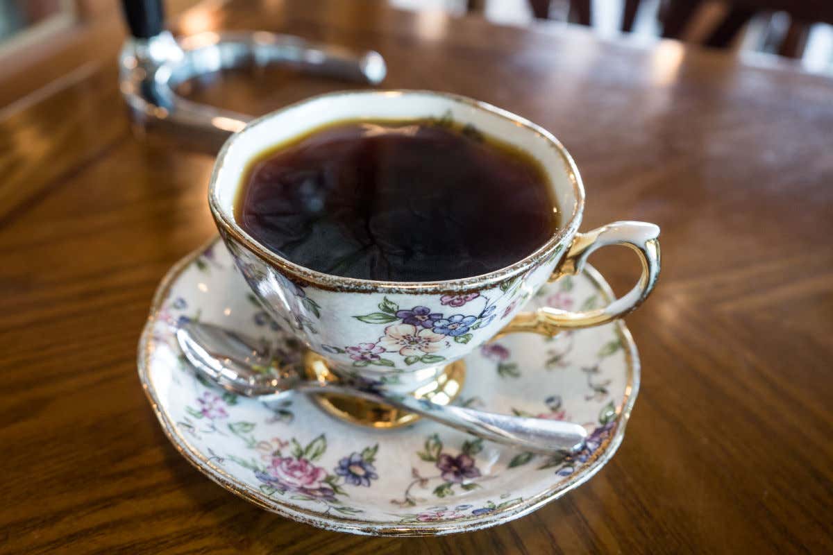 Una taza de porcelana con decoración floral y rellena de café sobre una mesa de madera