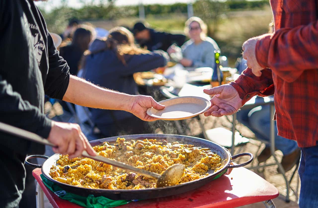 Un hombre repartiendo la típica paella valenciana