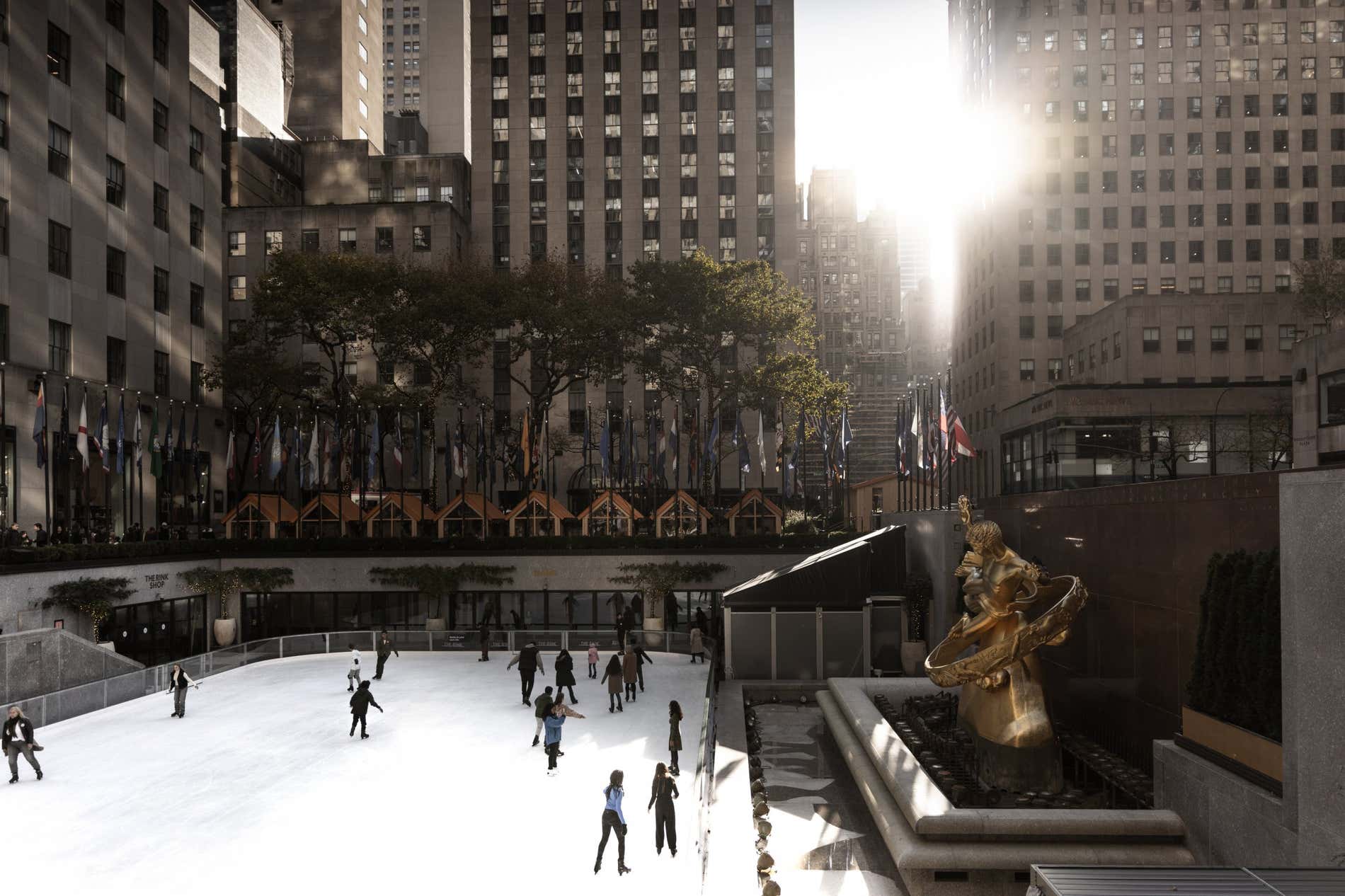 Rockefeller Center Ice Rink full of people ice skating with the sun shining between the buildings