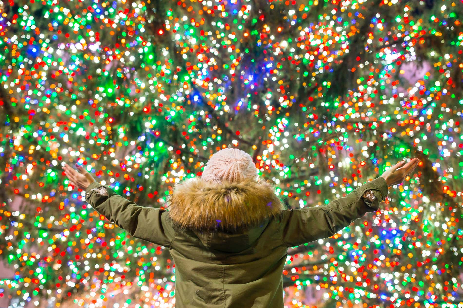 Someone with a winter coat and a fluffy hat checking out the Rockefeller center christmas lights on the christmas tree