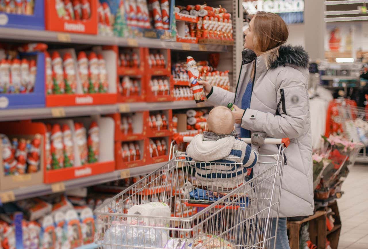 Una madre con su bebé cogiendo un Papá Noel de chocolate y comprando dulces navideños en un supermercado