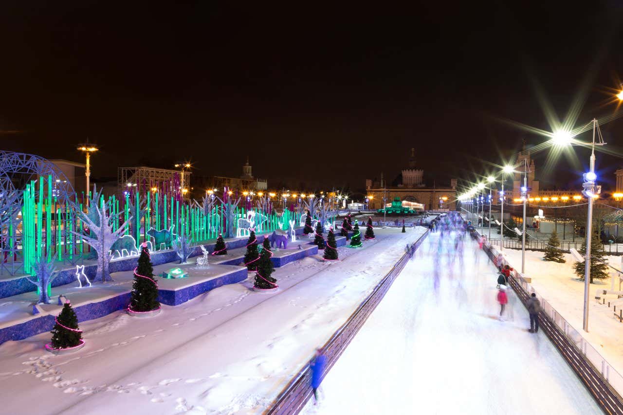 VDNKh Ice Rink in Moscow at night with snow on the ground around the ice rink and christmas decorations all around.
