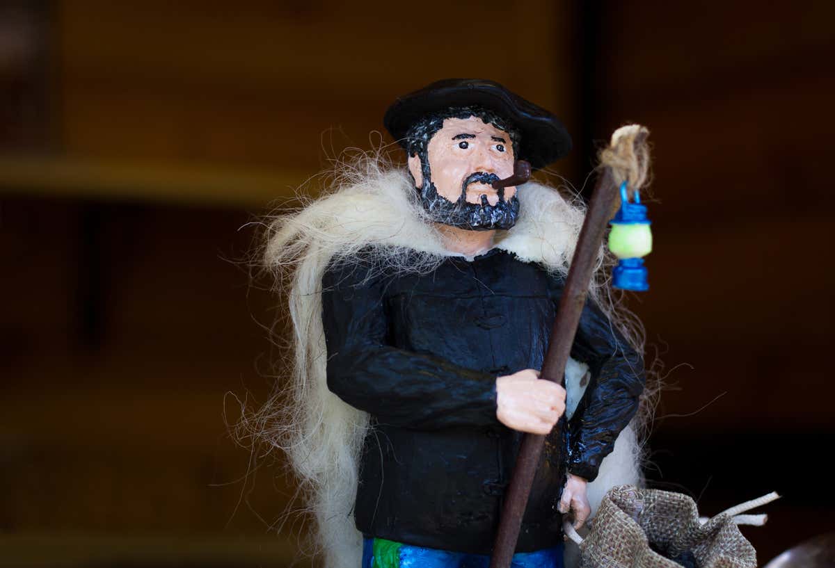 Figura de un Olentzero, un hombre robusto que tiene una pipa en su boca, viste un abrigo grande y una chaqueta negra.