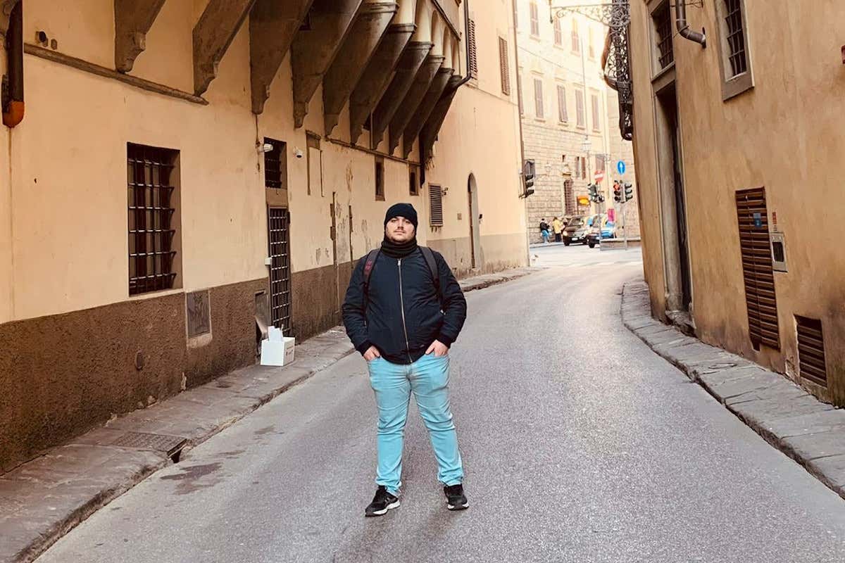 Un hombre posando para una foto en una calle histórica de edificios color crema