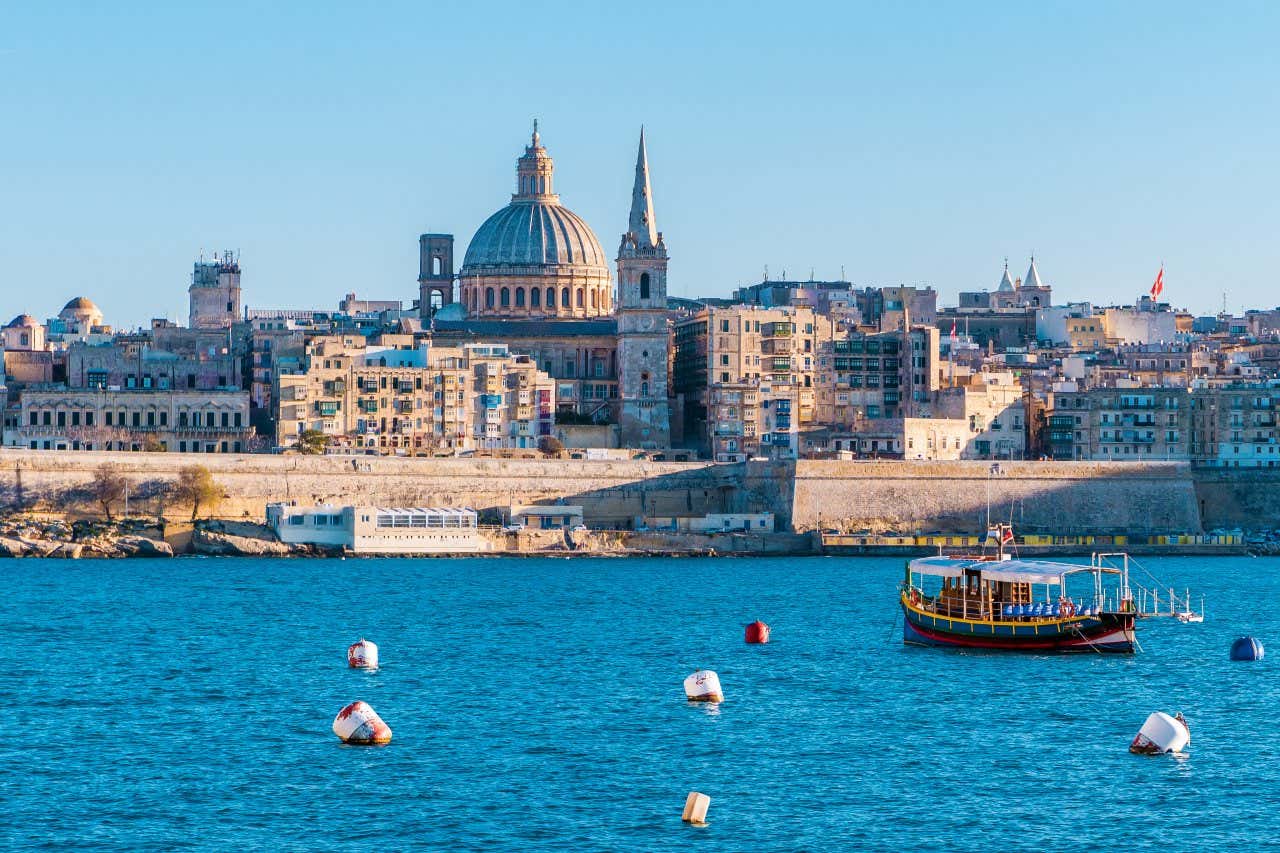 Vista de antigos palácios barrocos e uma cúpula em meio aos edifícios no centro de Valletta, a capital de Malta e, no mar, uma embarcação