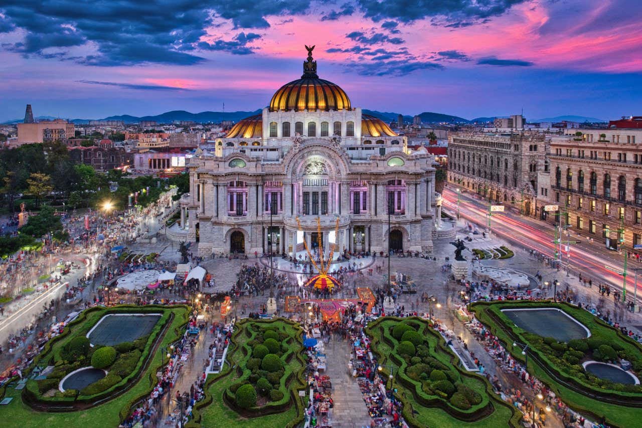 The Palace of Fine Arts in Mexico City at sunset, a neoclassical palace with many people outside during a market.