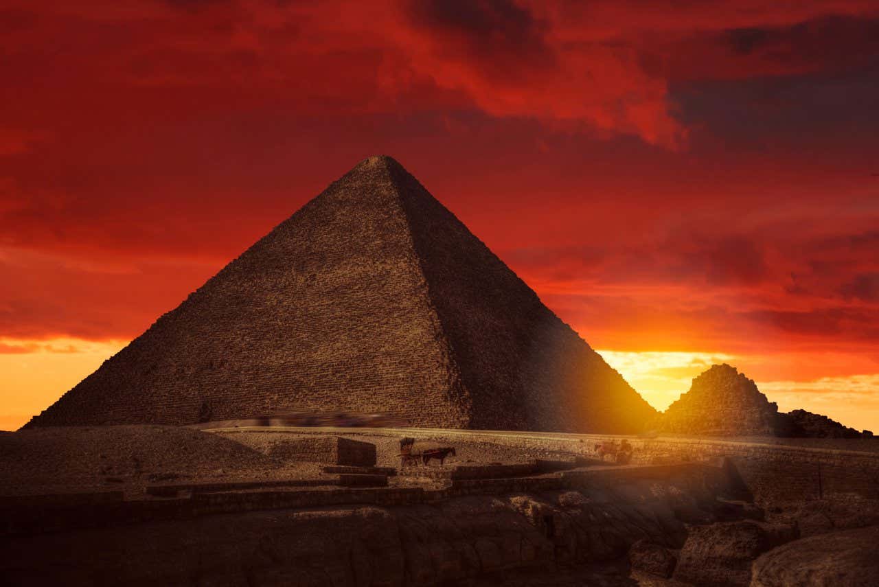 La Grande Pyramide de Gizeh vue du sol alors que le soleil se couche, donnant au désert une teinte orange foncé