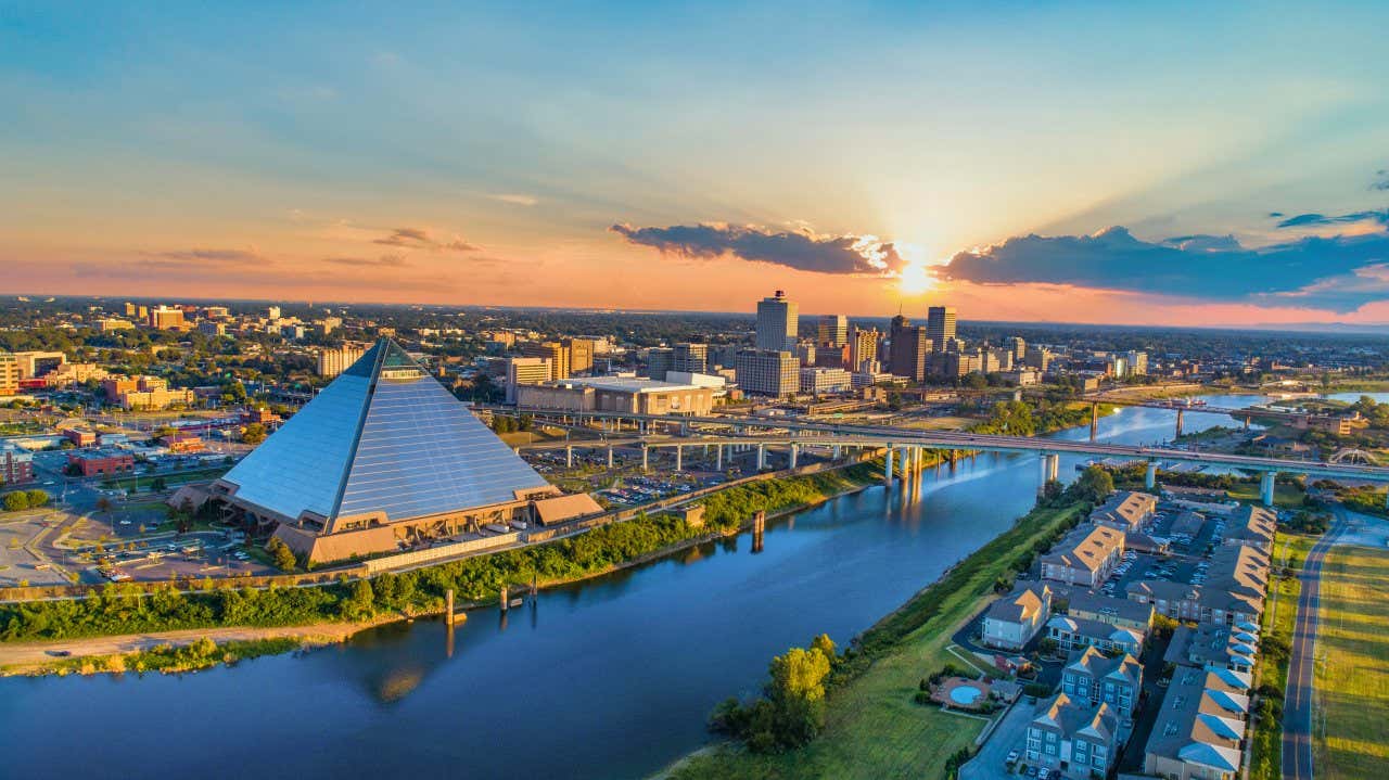 Vue aérienne de la pyramide de Memphis depuis l'autre côté d'une rivière au coucher du soleil, avec Memphis visible à l'arrière-plan