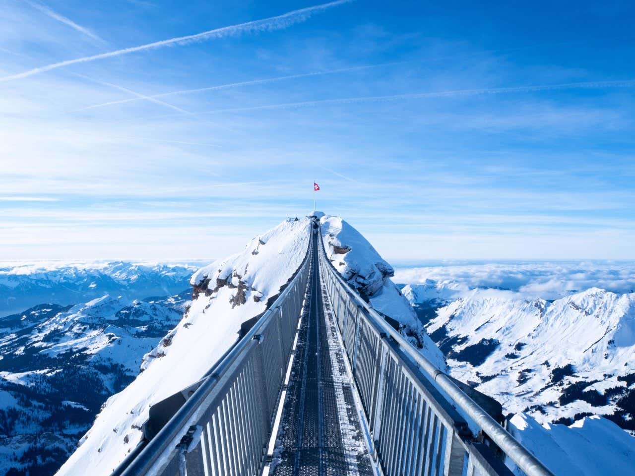 Peak Walk by Tissot footbridge on Glacier 3000 with the Swiss flag at the top and a breathtaking view of the surrounding snow-capped mountains