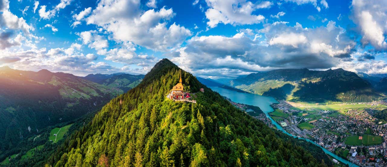 View of Harder Kulm under a blue sky dotted with small clouds, with the lake and town of Interlaken below