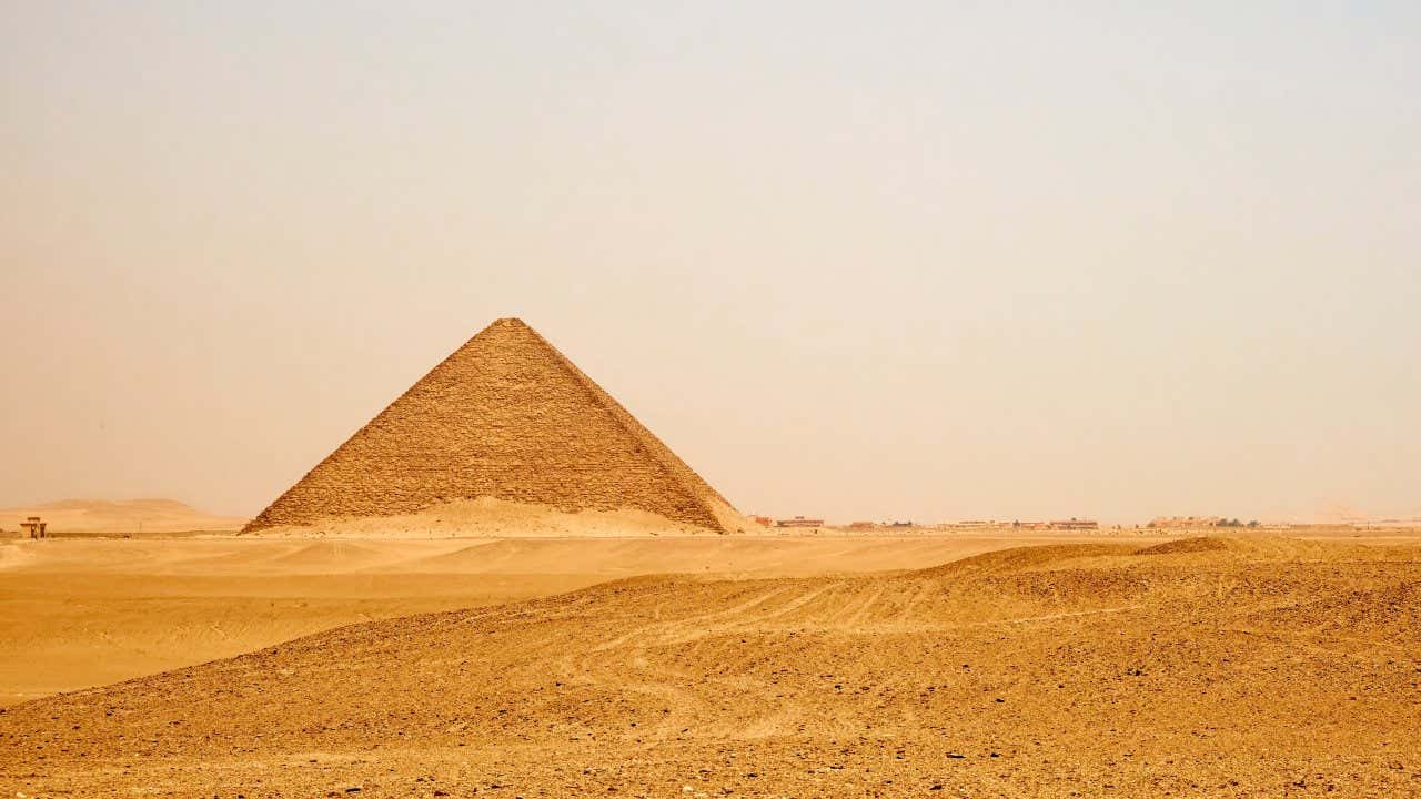 La pyramide rouge vue de loin un jour de faible visibilité, avec des traces visibles dans le sable du désert au premier plan
