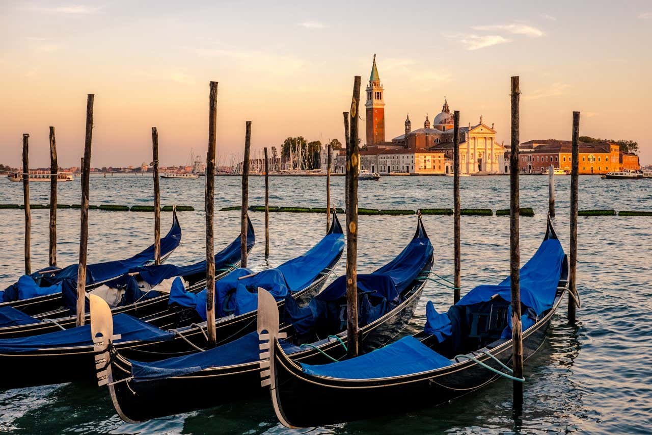 Five blue gondolas docked at a small pier with the palaces of central Venice in the background.