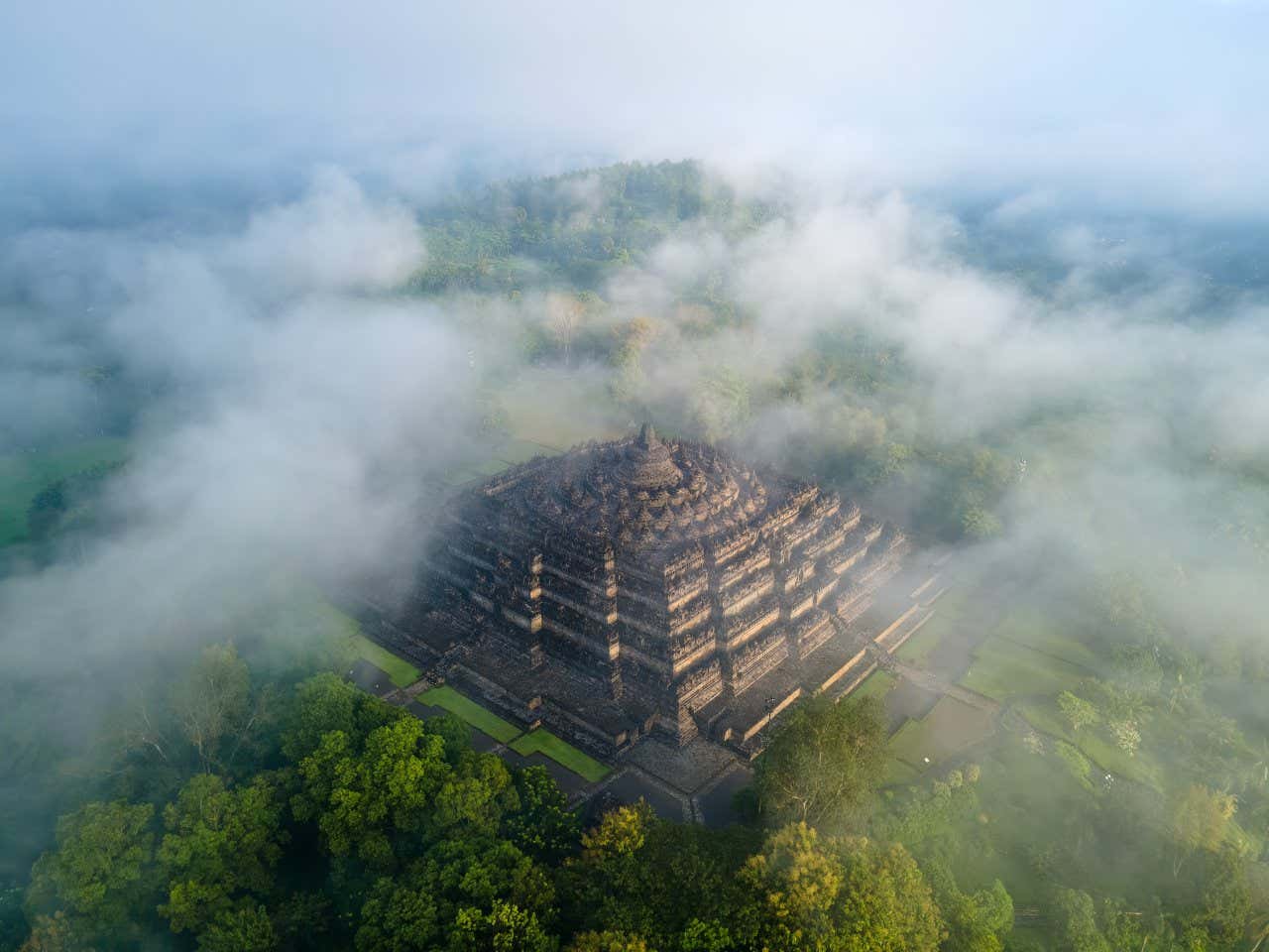 Le temple de Borobudur vu d'en haut, les nuages recouvrant partiellement le temple et la forêt qui l'entoure