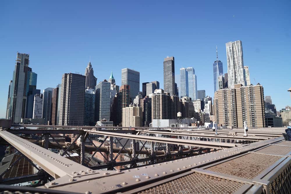 Dai tralicci superiori in ferro del Ponte di Brooklyn, una foto ai grattacieli di New York in una giornata di sole