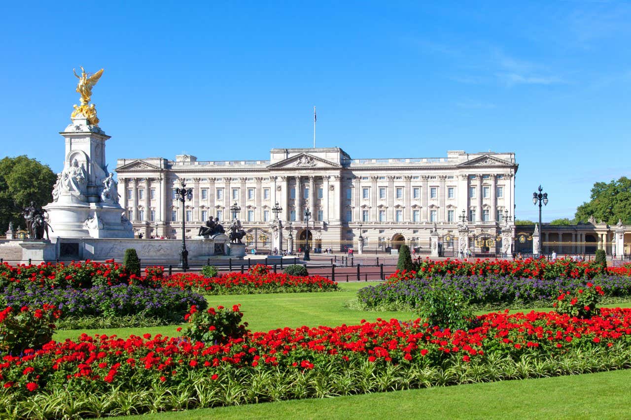 Panorâmica do Palácio de Buckingham com os jardins reais à frente repleto de flores vermelhas