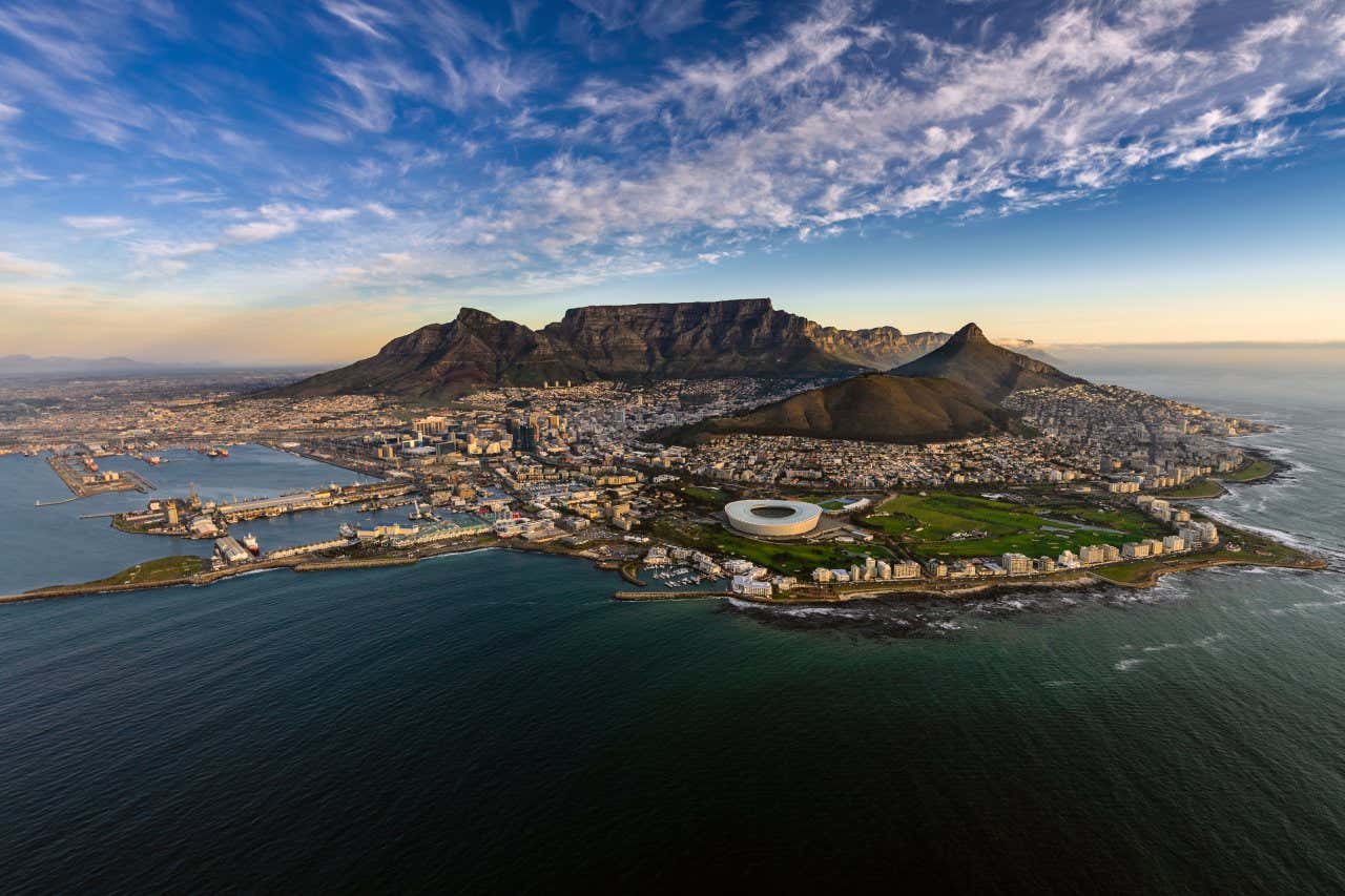 An aerial view of Cape Town with Table Mountain in the background on a clear day with some fluffy clouds in the sky.