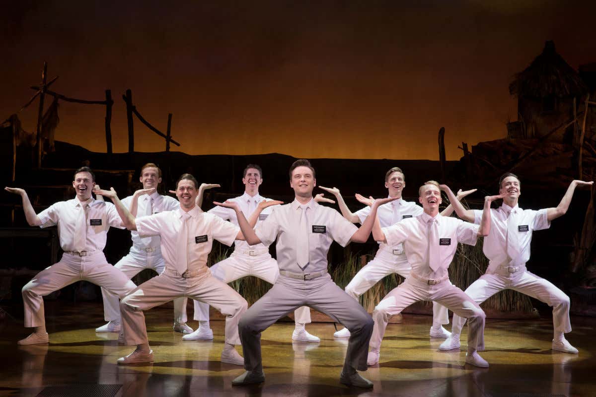 Bailarines vestidos completamente de blanco subidos a un escenario de teatro representando The Book of Mormon