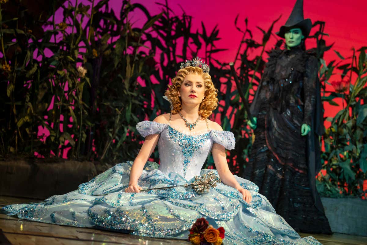 Una bruja de piel verde ataviada con un traje negro contemplando a una princesa durante el musical de Wicked en Nueva York