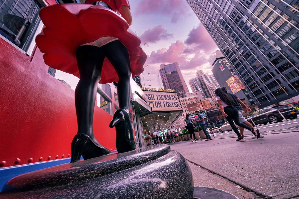 Escultura de una mujer con un vestido corto frente a los rascacielos de Nueva York