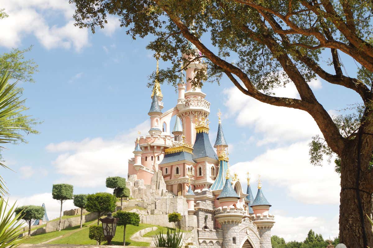 Sleeping Beauty Castle at Disneyland Paris with pink and blue turrets and surrounded by trees
