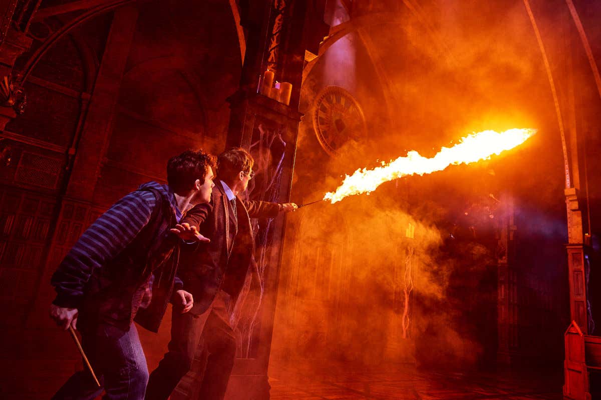 Dos adultos con varitas mágicas creando fuego en mitad de un escenario de teatro