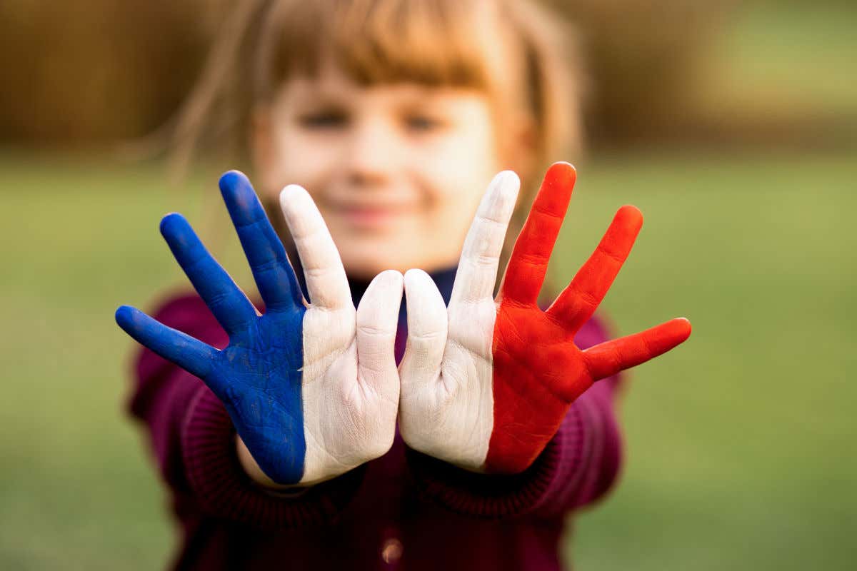 A girl holds up her hands painted in the colors of the French flag, her face blurry out of focus