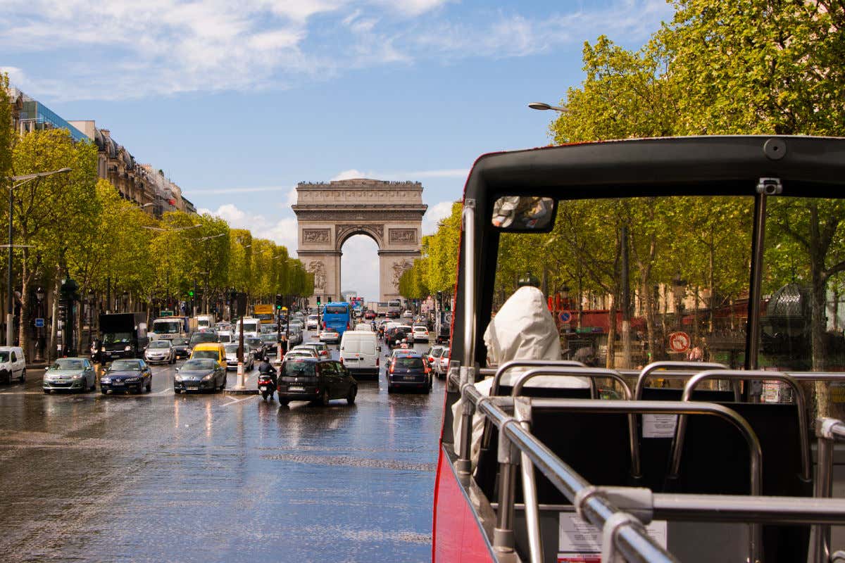 Second floor of a convertible bus driving along the Champs Elysées with the Arc de Triomphe in front of it