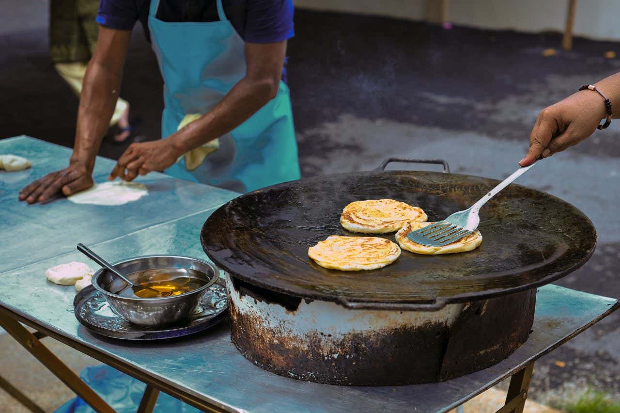 2 people cooking bread at an Indian street food stall, 1 person kneading dough, the other frying it.