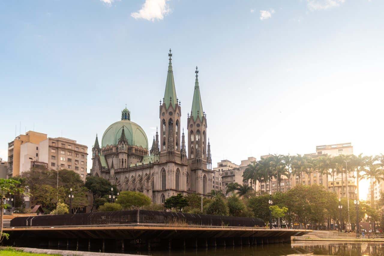 Panorâmica lateral da Catedral da Sé em São Paulo rodeada de árvores e edifícios ao entardecer