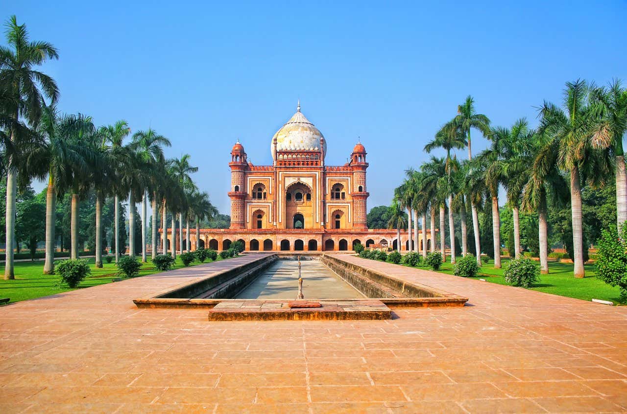 The Taj Mahal as seen from afar, with a clear blue sky in the background and trees lining the avenue in front.