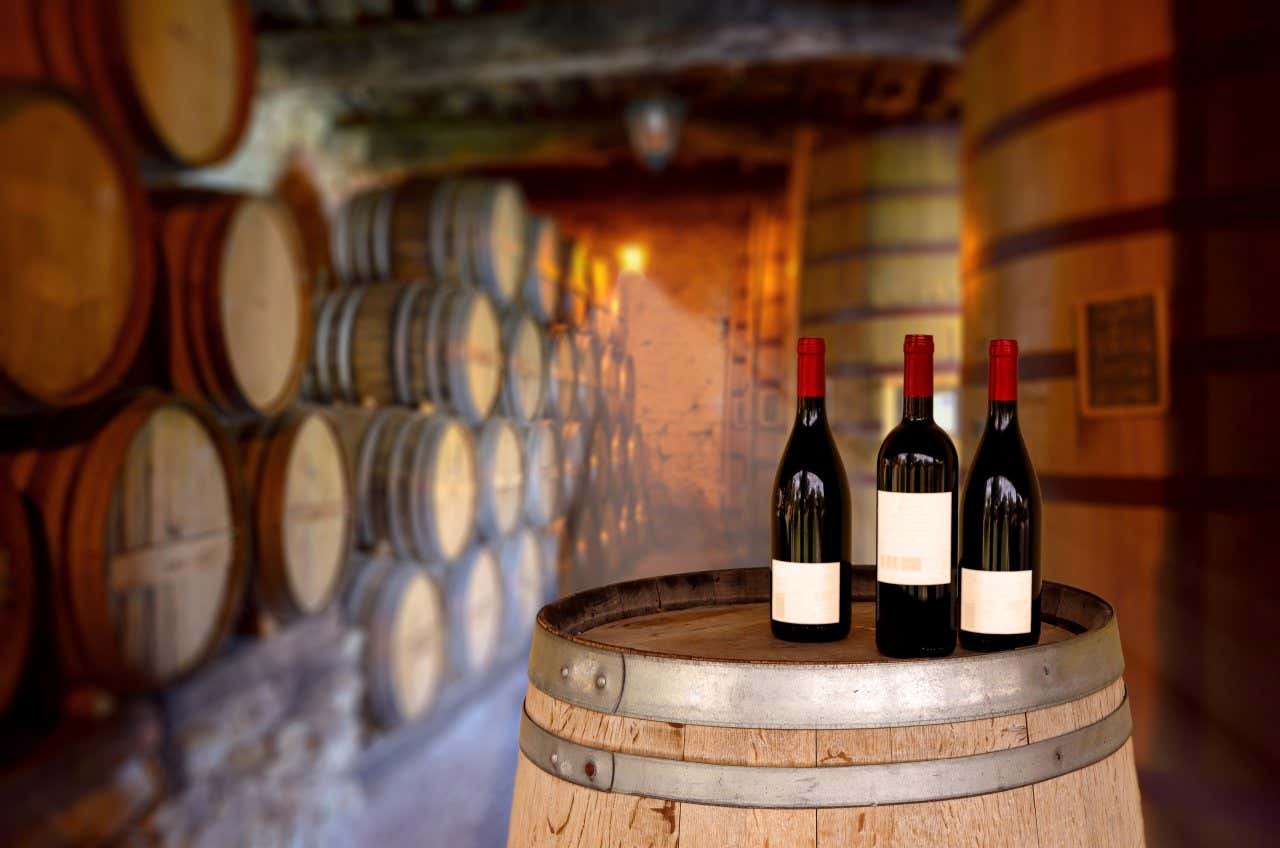 3 bottles of red wine on a barrel in a winery