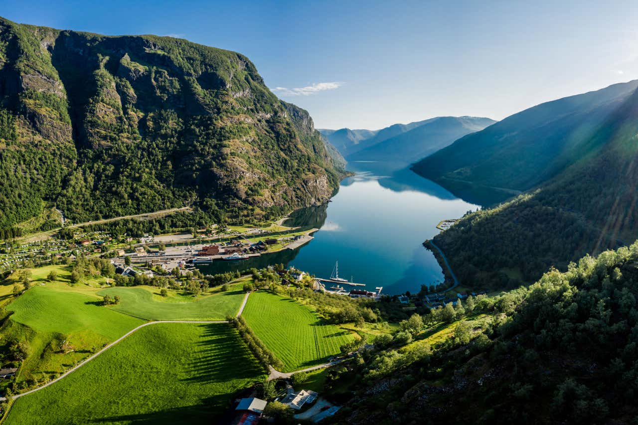 Vue aérienne sur les eaux d'un fjord entre de hautes montagnes et un village avec un port et des bateaux