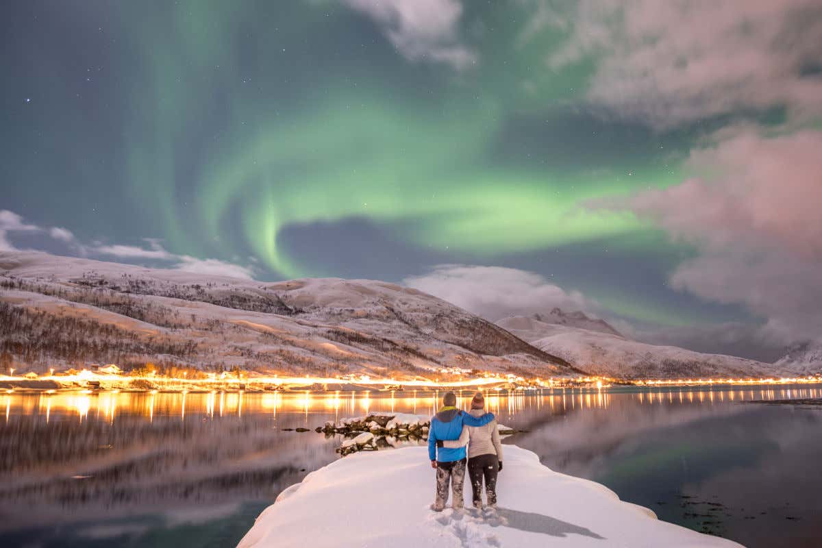 Un couple de dos à l'appareil photo, regardant les montagnes enneigées et les aurores boréales