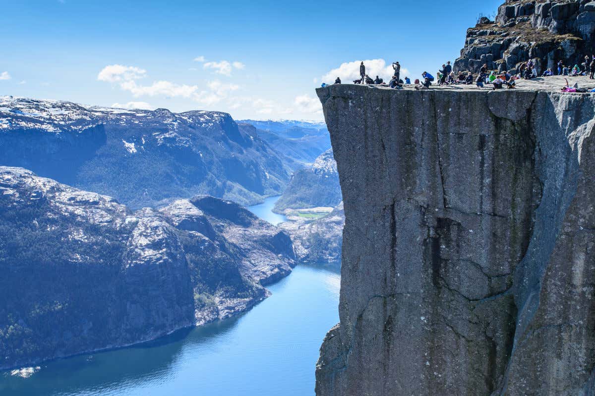 Touristes au sommet d'une falaise surplombant les montagnes enneigées de Norvège et un fjord
