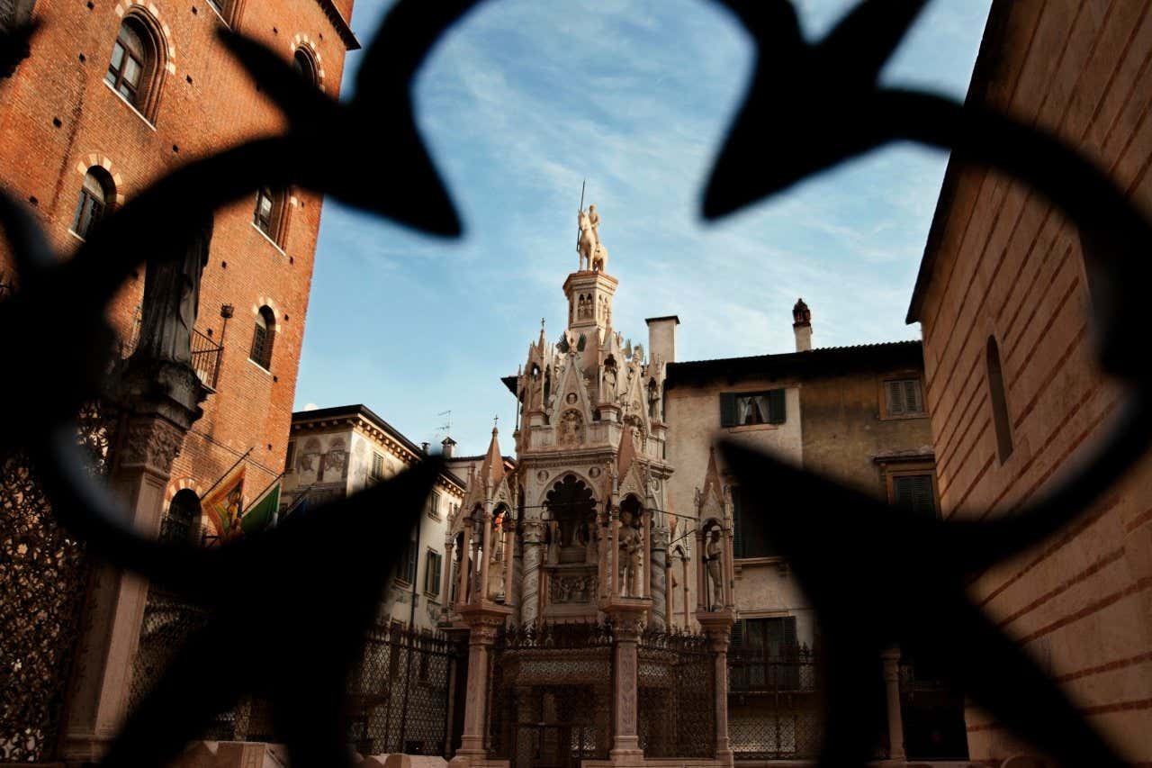 A view of the Church of Santa Maria Antica through a black gate under a blue sky.